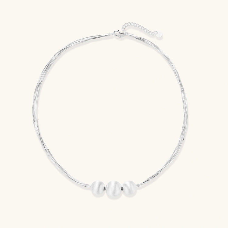 Sterling silver multi-strand necklace with three brushed round beads on cream background