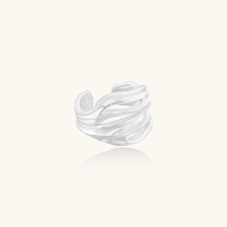 Wide sterling silver cuff ring with flowing wave patterns creating dimensional texture against cream background