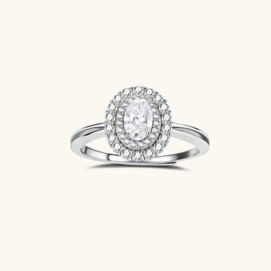 Sterling silver ring with oval moissanite center stone surrounded by double halo of sparkling stones on neutral background.