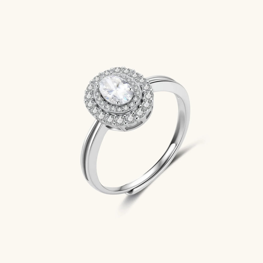 Sterling silver ring with oval moissanite center stone surrounded by double halo of sparkling stones on neutral background.