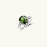 White gold plated jewelry set with green teardrop gemstones and cubic zirconia halos on cream background.