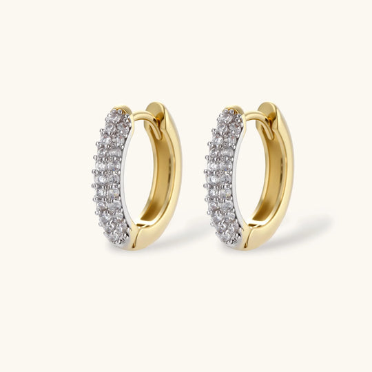 Gold-plated curved necklace, hoop earrings, and adjustable ring with pavé cubic zirconia stones on cream background.