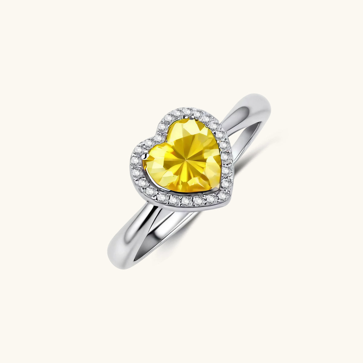 Heart-shaped yellow moissanite ring with diamond halo in sterling silver setting on neutral background
