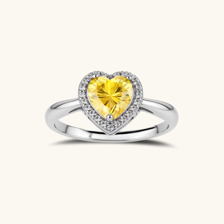 Heart-shaped yellow moissanite ring with diamond halo in sterling silver setting on neutral background