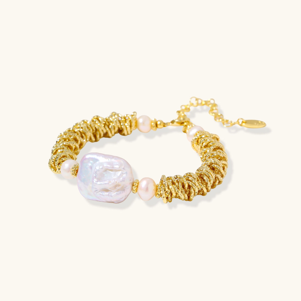 18k gold-plated bracelet with textured wave segments, baroque pearl centerpiece, and round freshwater pearls on cream background