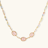 Gold necklace with three rose quartz stones, multicolor pastel beads, and pearl accents on white background.