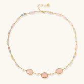Gold necklace with three rose quartz stones, multicolor pastel beads, and pearl accents on white background.