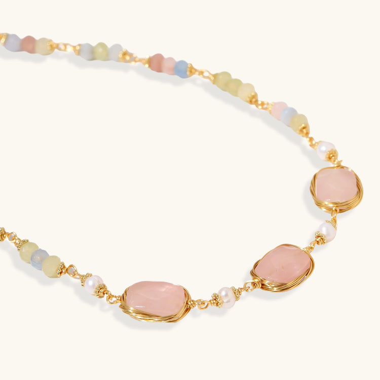 Gold necklace with three rose quartz stones, multicolor pastel beads, and pearl accents on white background.
