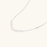 Delicate sterling silver chain necklace with small freshwater pearls arranged in a curved smile arc on cream background.