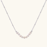 Delicate sterling silver chain necklace with small freshwater pearls arranged in a curved smile arc on cream background.