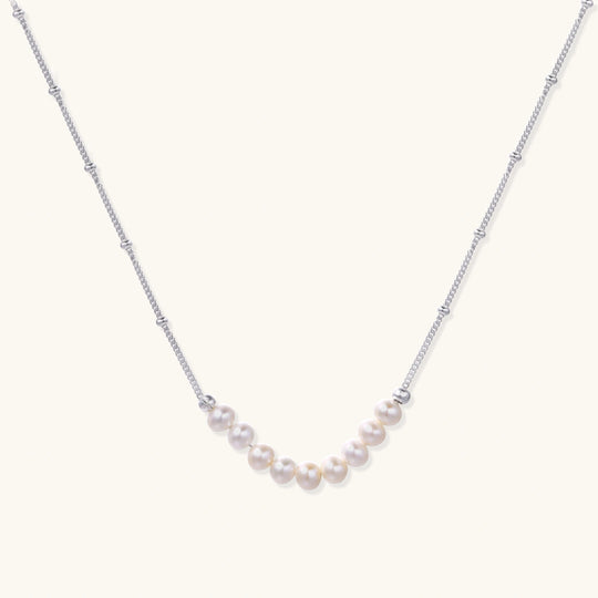 Delicate sterling silver chain necklace with small freshwater pearls arranged in a curved smile arc on cream background.