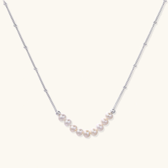 Delicate sterling silver chain necklace with small freshwater pearls arranged in a curved smile arc on cream background.