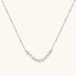 Delicate sterling silver chain necklace with small freshwater pearls arranged in a curved smile arc on cream background.