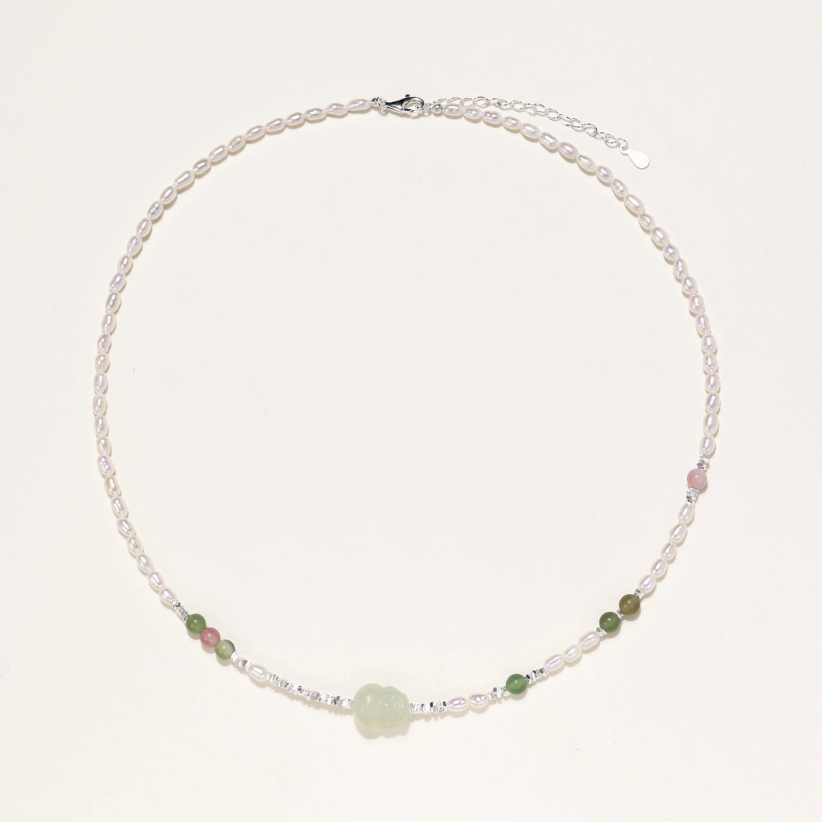 Delicate pearl necklace with pale green serpentine jade centerpiece and colorful agate beads on cream background