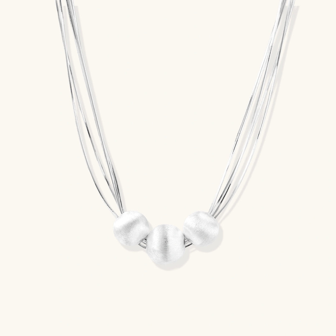 Sterling silver multi-strand necklace with three brushed round beads on cream background