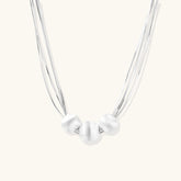 Sterling silver multi-strand necklace with three brushed round beads on cream background
