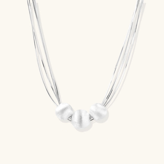Sterling silver multi-strand necklace with three brushed round beads on cream background