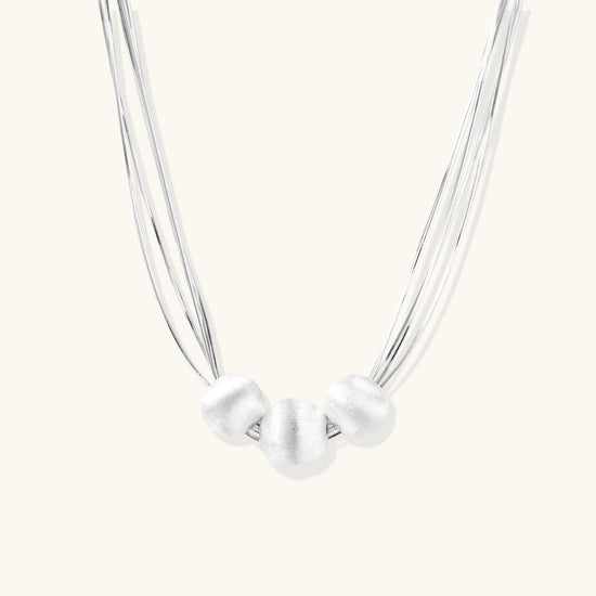 Sterling silver multi-strand necklace with three brushed round beads on cream background