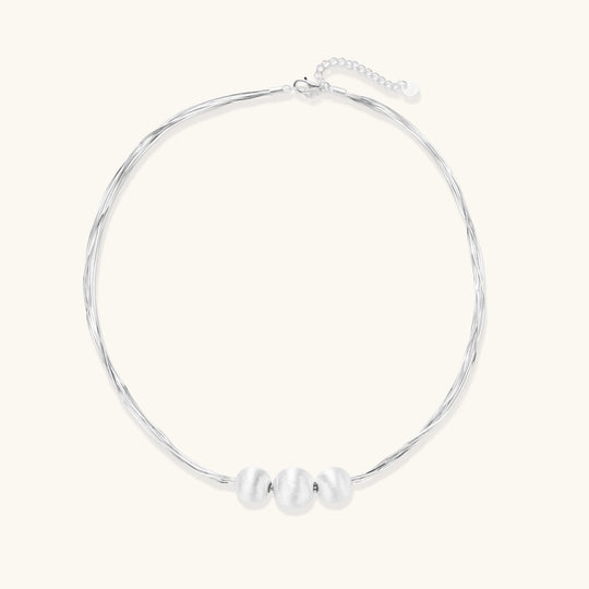 Sterling silver multi-strand necklace with three brushed round beads on cream background