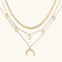 Four-layer gold necklace with herringbone chain, disc charms, and crescent moon pendant on cream background
