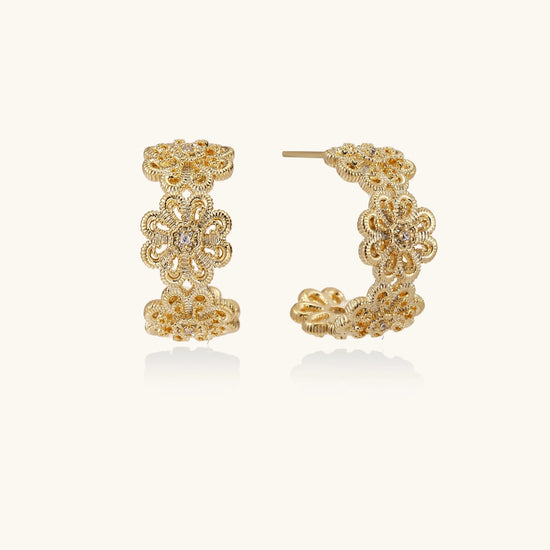 Gold hoop earrings with intricate three-dimensional floral filigree pattern in 14K gold plated brass on cream background