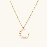 Gold crescent moon pendant with graduated white pearls on delicate chain against cream background