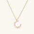 Gold crescent moon pendant with graduated white pearls on delicate chain against cream background