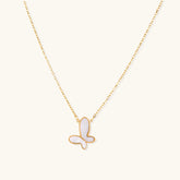 Gold-plated butterfly pendant with iridescent mother of pearl inlay on delicate chain against cream background.