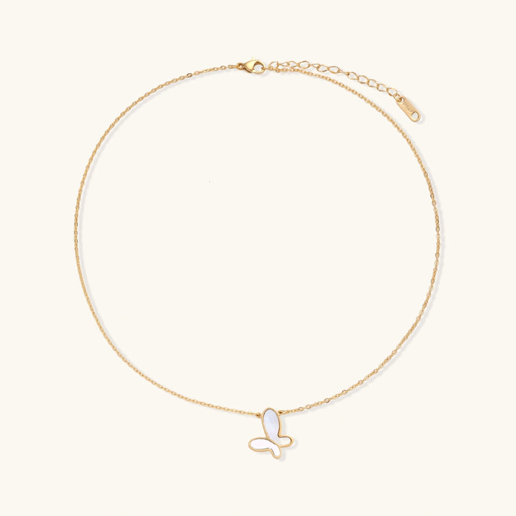 Gold-plated butterfly pendant with iridescent mother of pearl inlay on delicate chain against cream background.