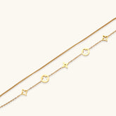 Double-layer gold-plated bracelet with quatrefoil and star charms on cream background, 18K gold finish.