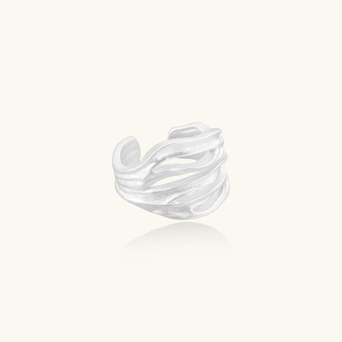 Wide sterling silver cuff ring with flowing wave patterns creating dimensional texture against cream background