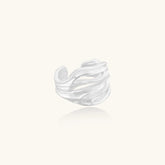 Wide sterling silver cuff ring with flowing wave patterns creating dimensional texture against cream background