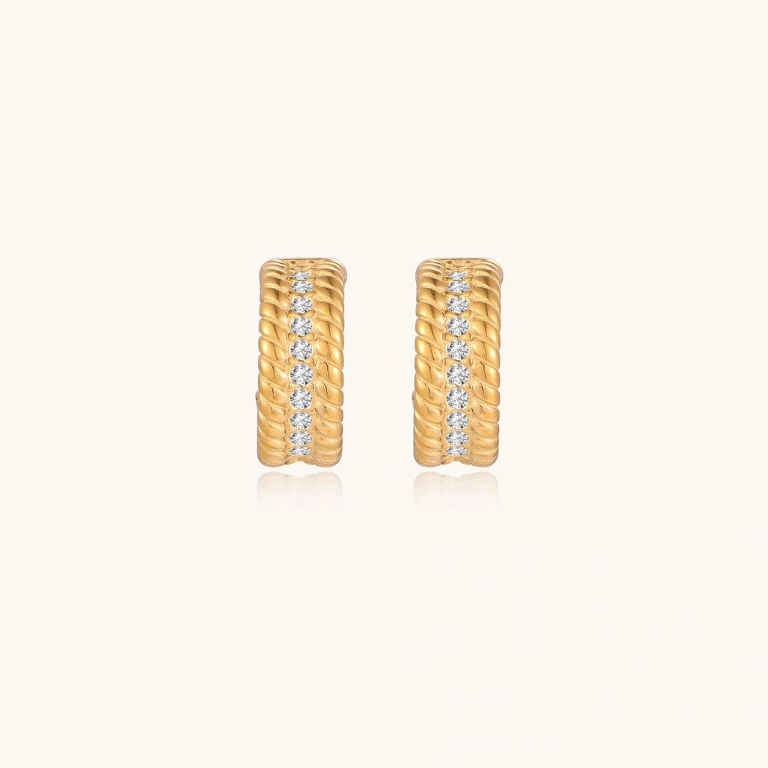 Textured gold huggie hoop earrings with raised ribbed rows creating dimensional sculptural design on cream background