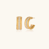 Textured gold huggie hoop earrings with raised ribbed rows creating dimensional sculptural design on cream background