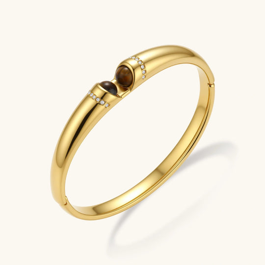 Polished gold bangle with two oval tiger's eye cabochons flanked by pavé diamond accents at center clasp.