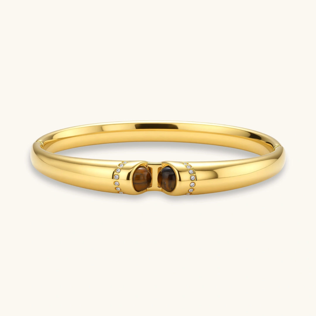 Polished gold bangle with two oval tiger's eye cabochons flanked by pavé diamond accents at center clasp.